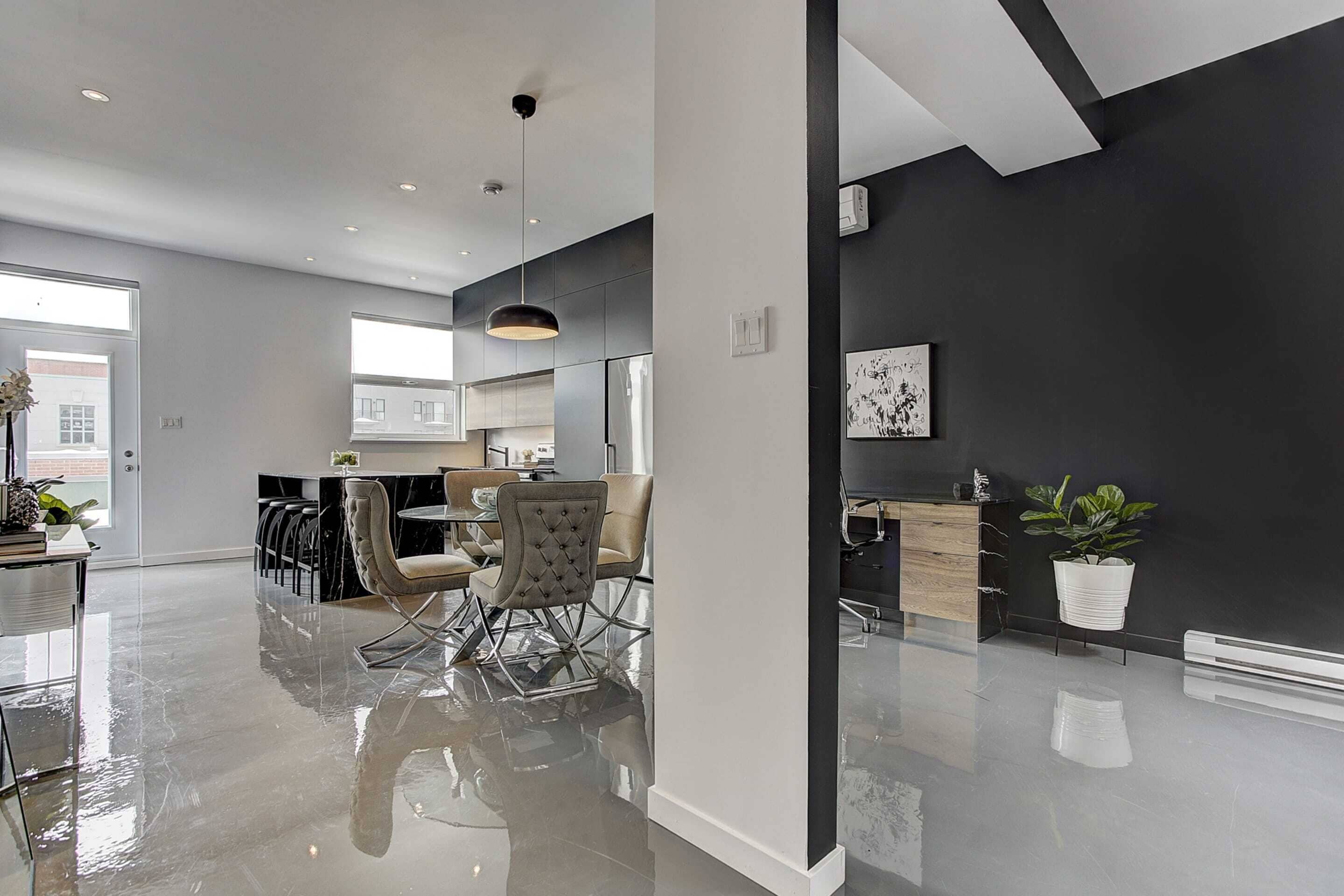 Une cuisine moderne avec un revêtement mural noir, des appareils en acier inoxydable et un coin repas comprenant une table en verre et des chaises rembourrées.