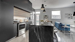 A modern kitchen with dark cabinetry, a marble island, and a blue sofa in the living area. - Les Lofts du Centre (Montreal)
