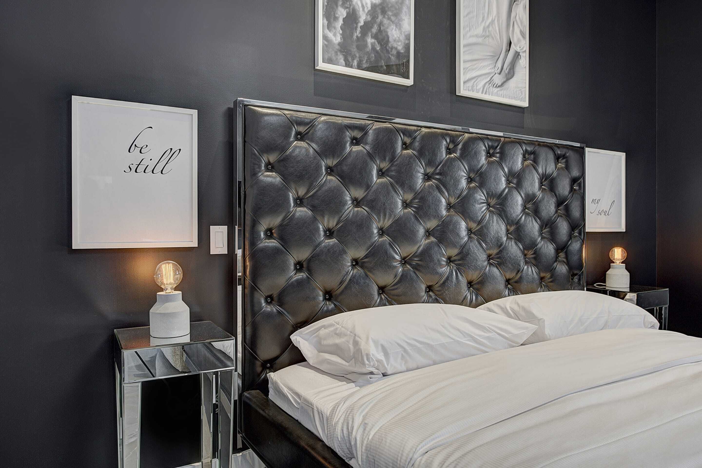 Un dormitorio moderno con cabecera capitonada, cama con ropa blanca y dos mesitas de noche con lámparas.