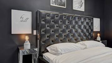 Un dormitorio moderno con cabecera capitonada, cama con ropa blanca y dos mesitas de noche con lámparas.
