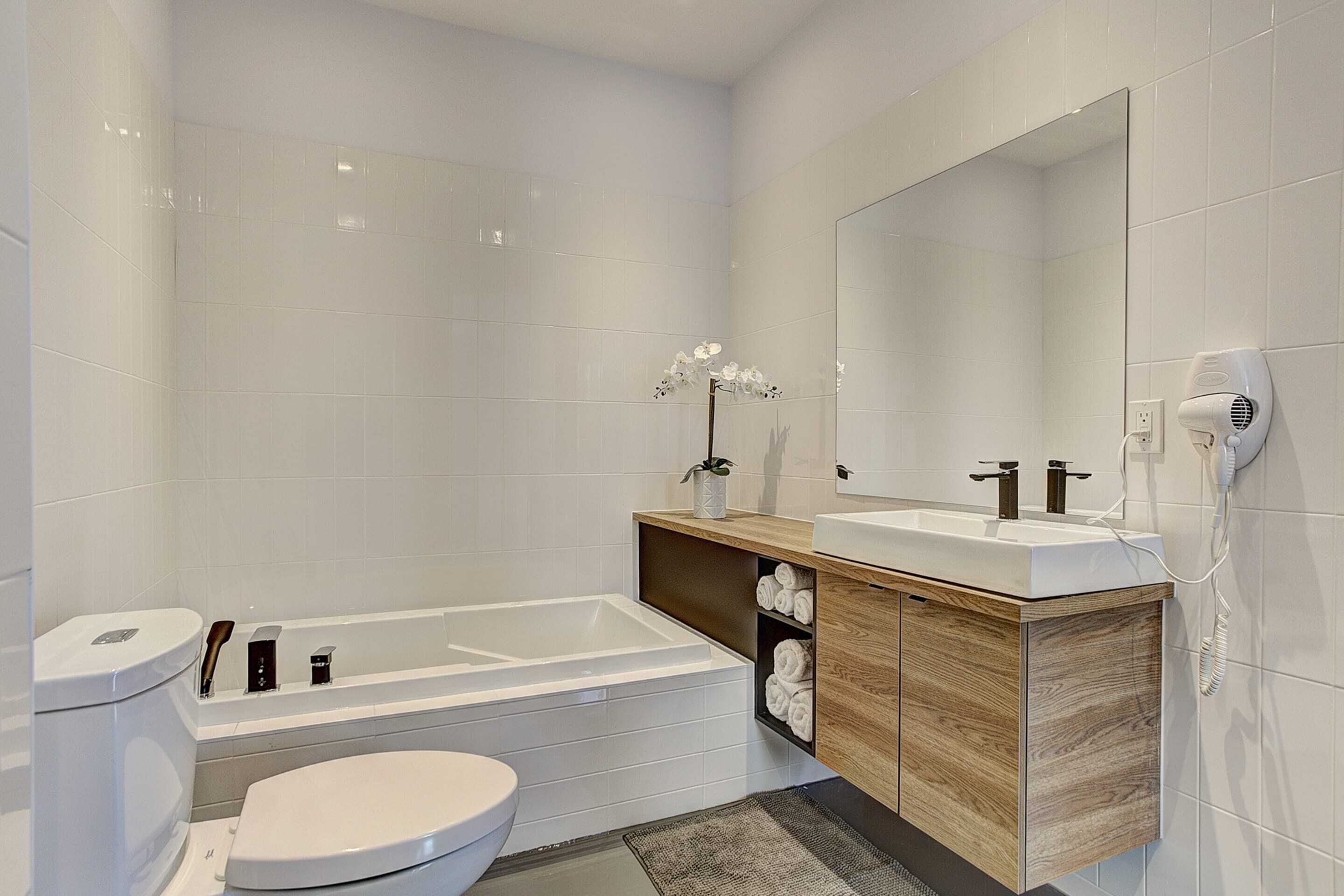 A modern bathroom with a bathtub, toilet, vanity with a mirror, and a towel rack.