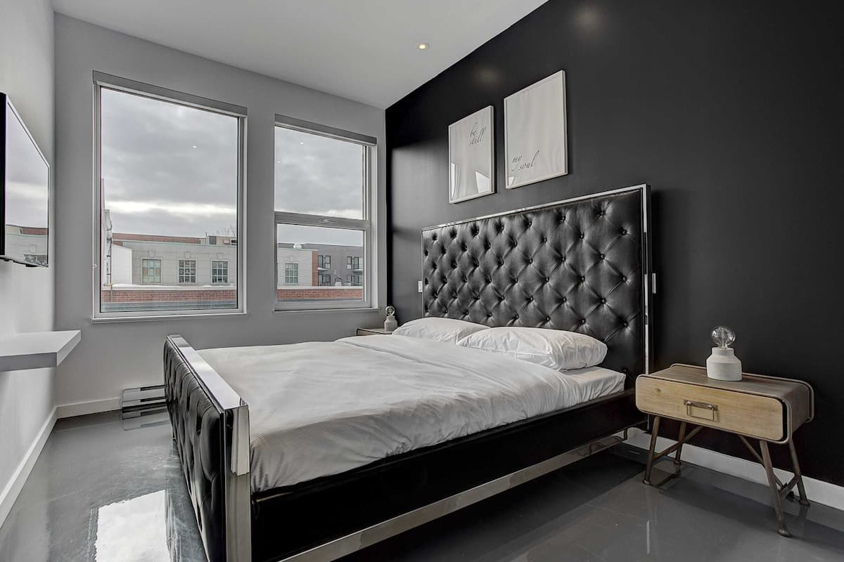 A modern bedroom with a large bed, a bedside table, and a view of the city through large windows.