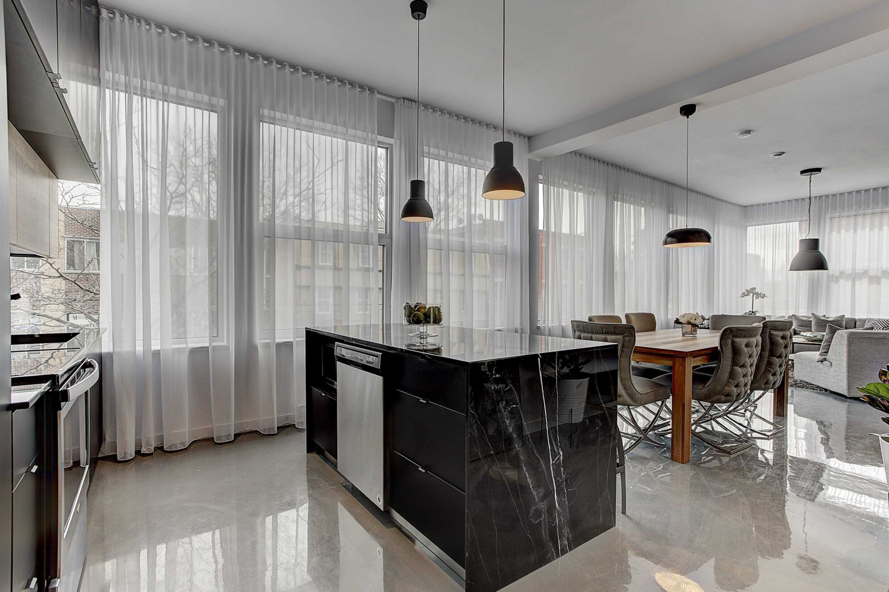 Eine moderne Küche mit einer schwarzen Marmorinsel, einem Essbereich mit Holztisch und -stühlen sowie einem Wohnbereich mit Sofa und Couchtisch.