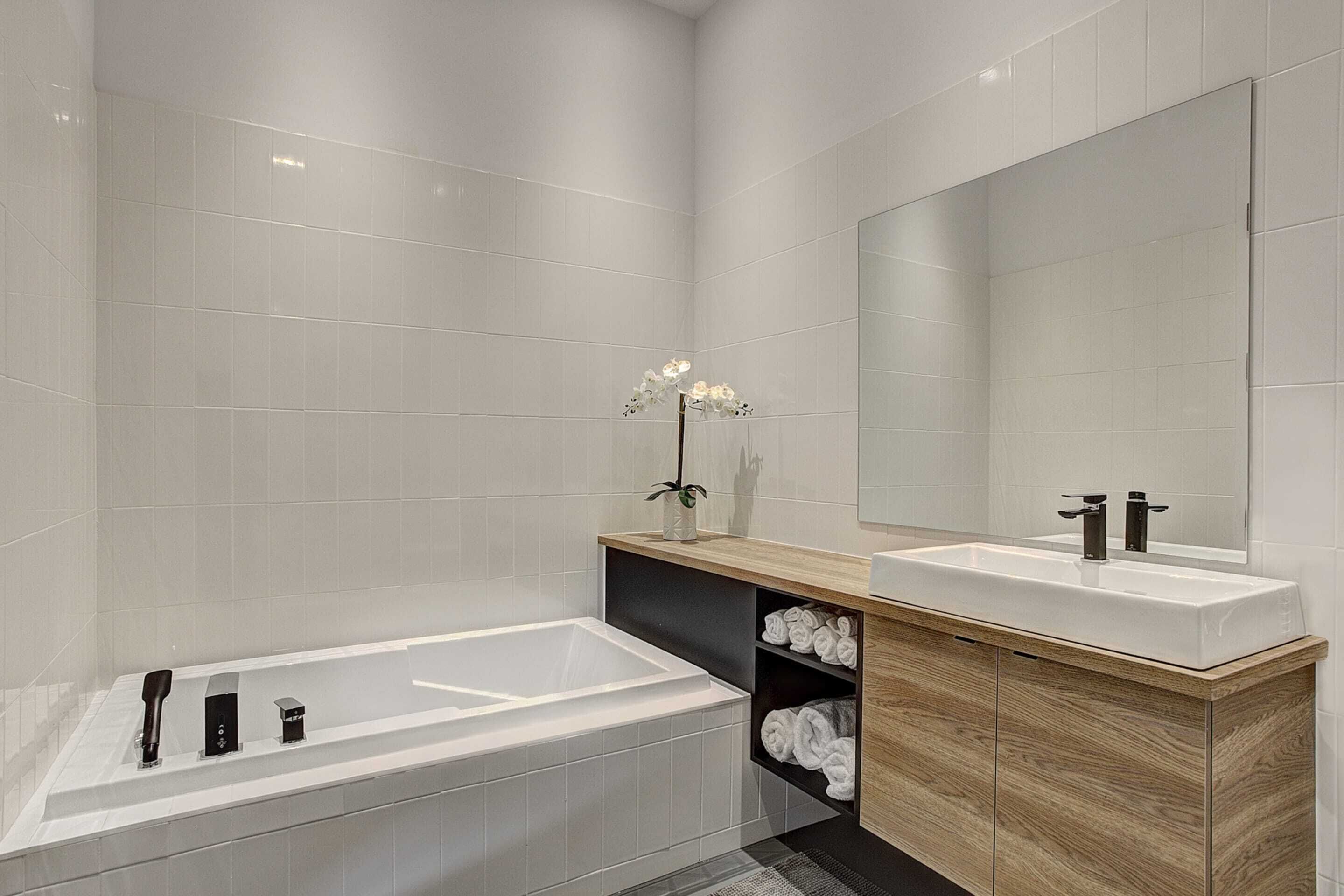 Un baño moderno con una bañera grande, dos lavamanos, un espejo y un estante con toallas.