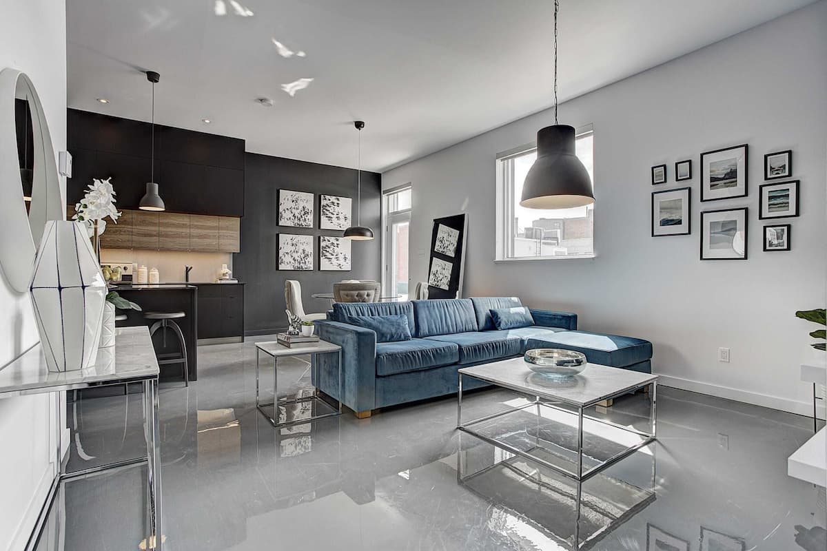 A modern living room with a blue sofa, a glass coffee table, and a kitchen area in the background.