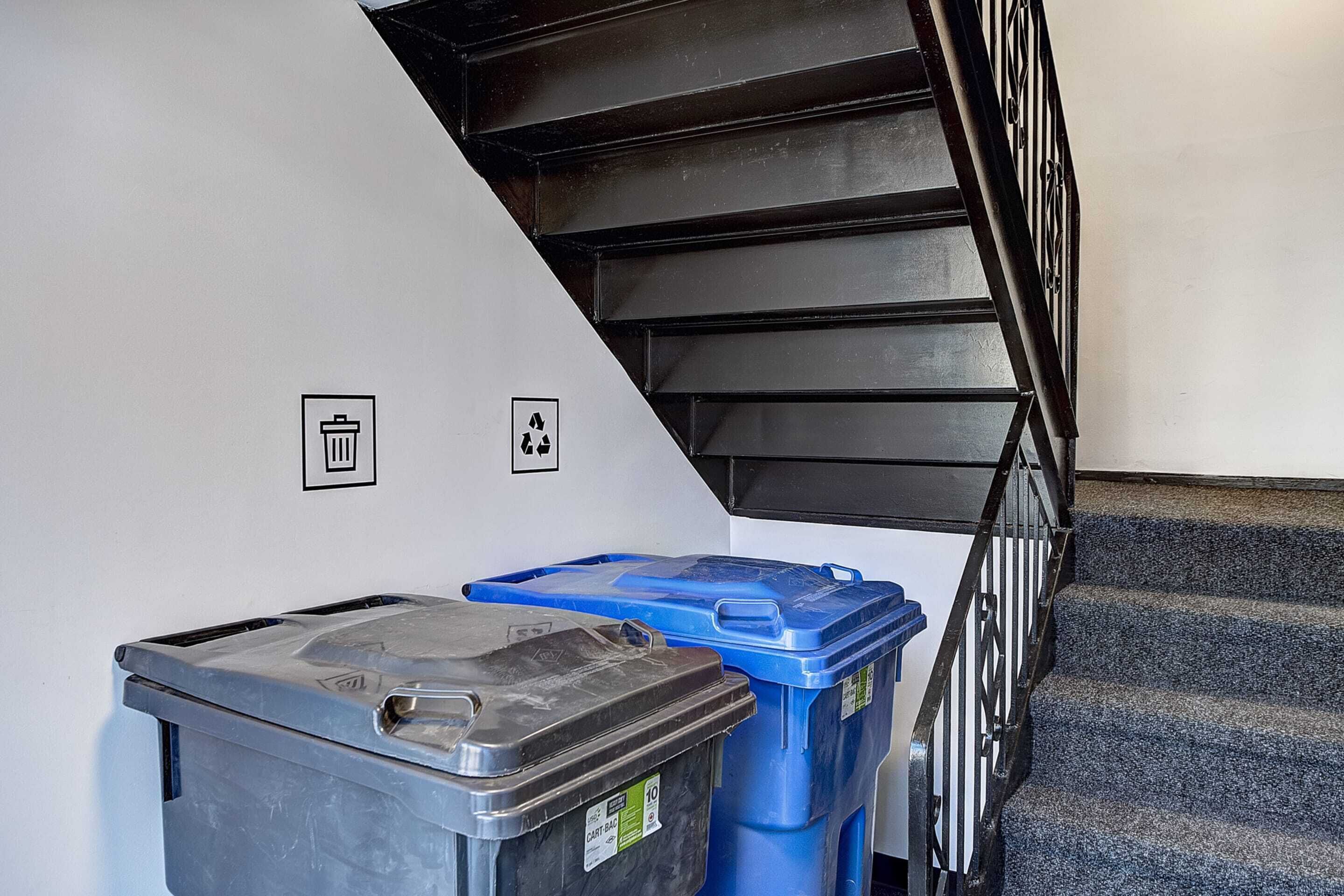 Una escalera con contenedores de basura y símbolos de reciclaje en la pared.