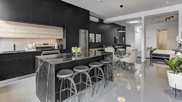 A modern kitchen with a marble island, bar stools, and a dining area with a chandelier. - Les Lofts du Centre (Montreal)