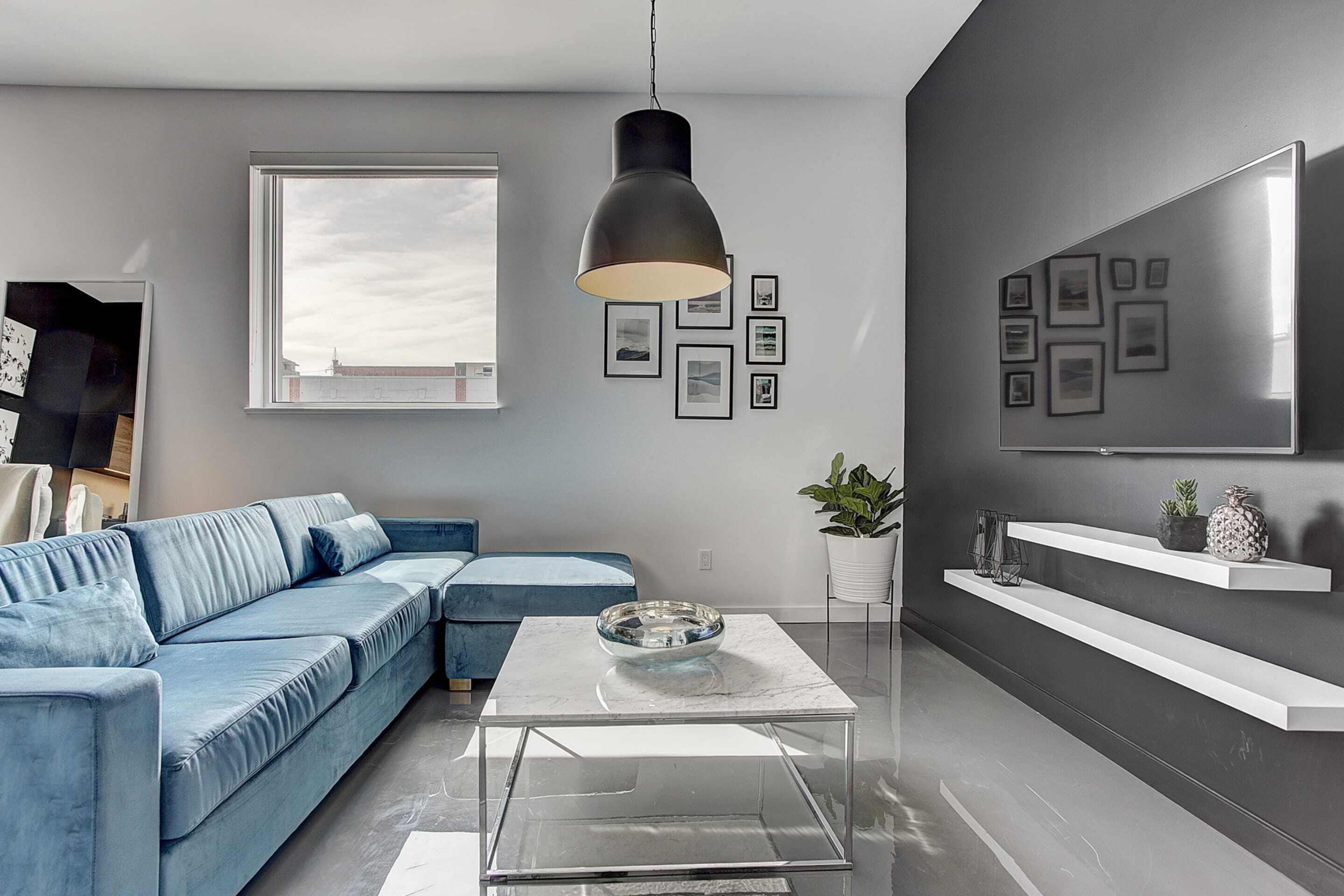 Una sala moderna con un sofá azul, una mesa de centro de vidrio y un ventanal grande.
