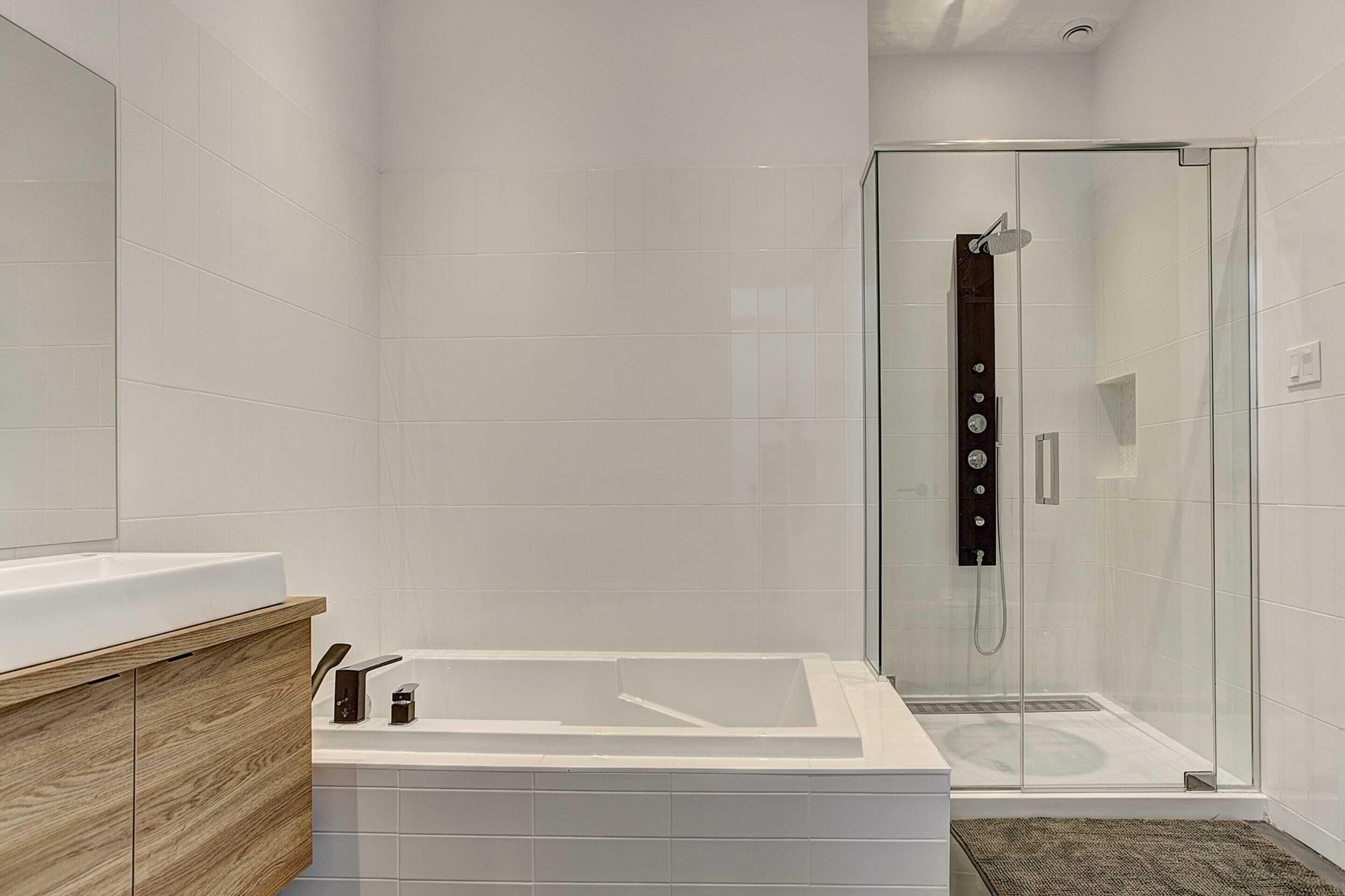 Un baño moderno con ducha envuelta en vidrio, una bañera blanca y un mueble de tocador de madera.