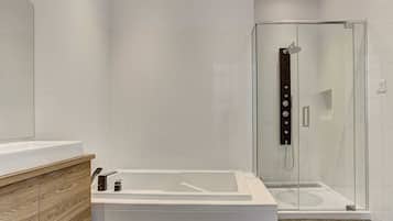 Un baño moderno con ducha envuelta en vidrio, una bañera blanca y un mueble de tocador de madera.