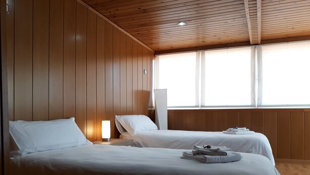 Hotellihuone, jossa on kaksi sänkyä, puupaneloidut seinät, suuri ikkuna ja yöpöytä, jossa on lamppu.