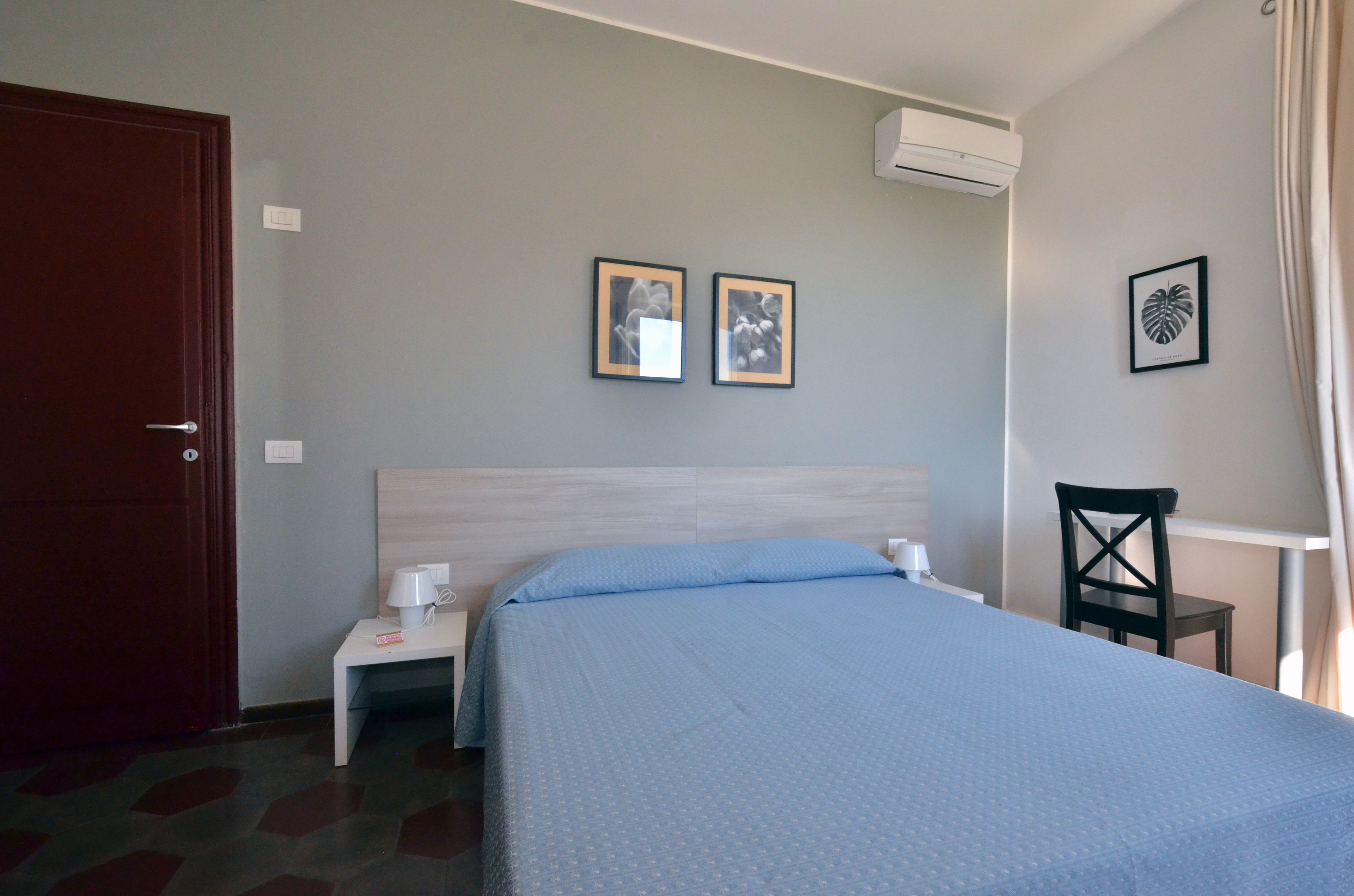 A hotel room with a bed, bedside table, lamp, chair, and two framed pictures on the wall.