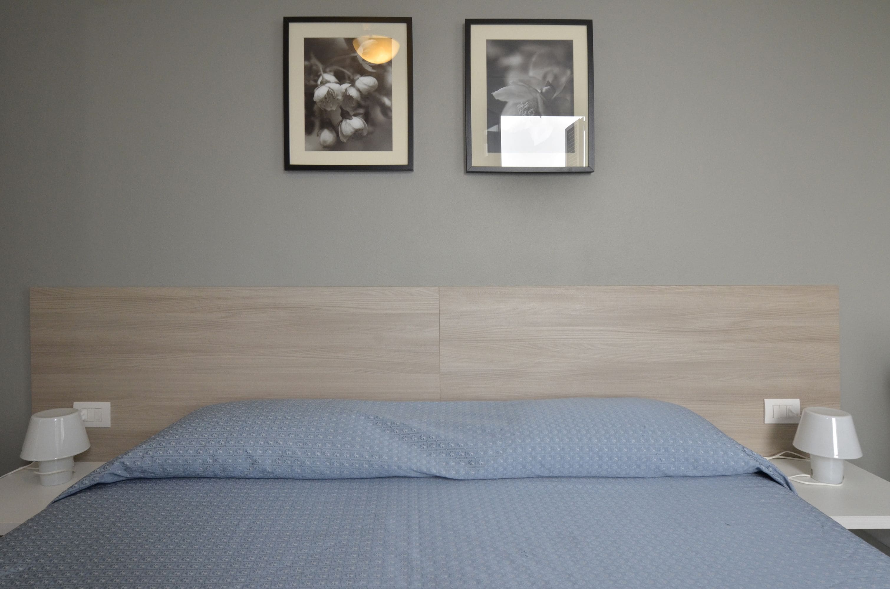 A neatly made bed with a blue patterned bedspread, two bedside lamps, and two framed pictures on the wall.