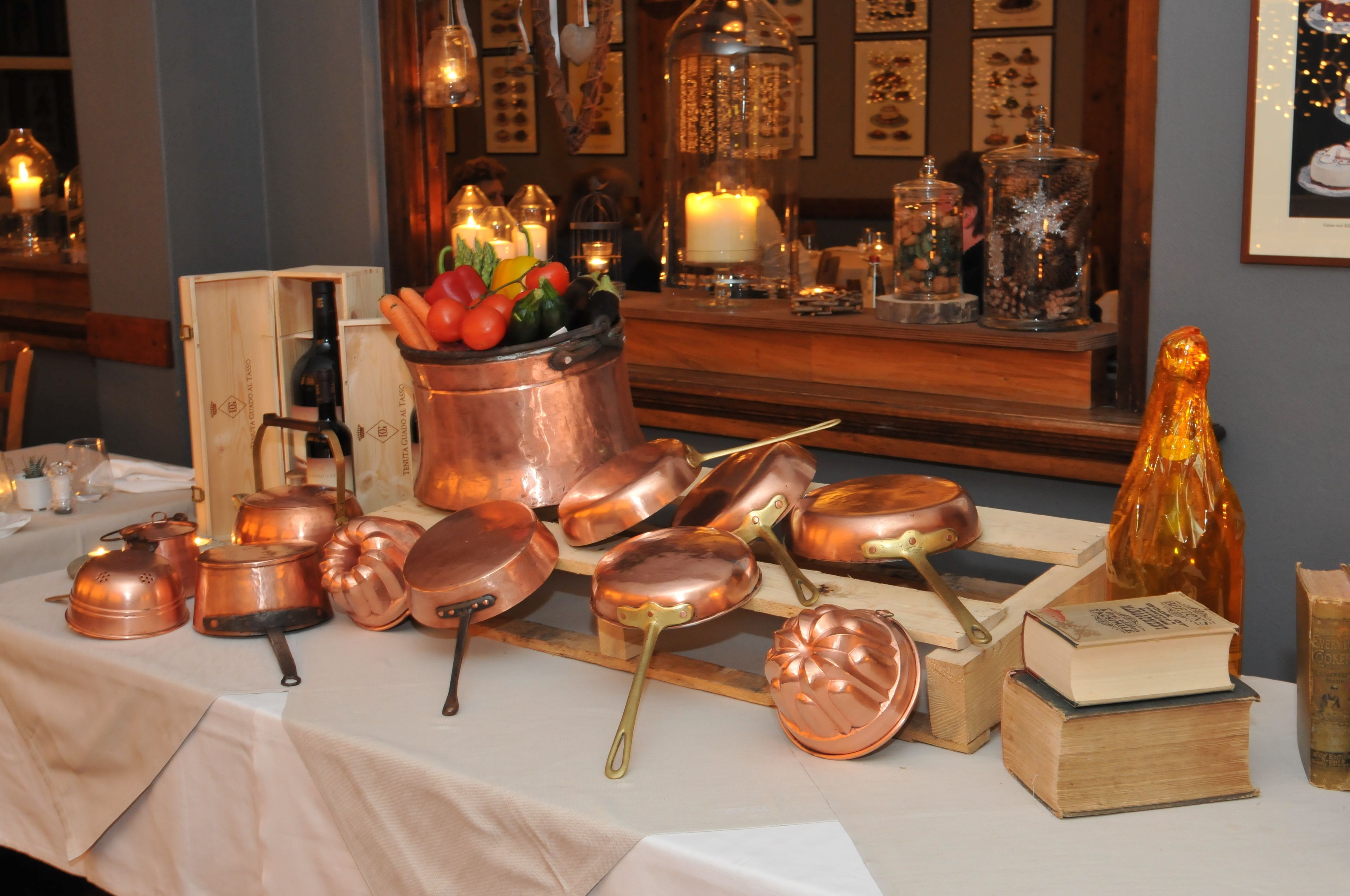 A display of copper cookware and a book on a table, with a candle and decorative items in the background.