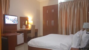 A hotel room with a bed, a desk, a chair, a television, and an air conditioning unit. - Kifina Emerald Hotel (Abuja)