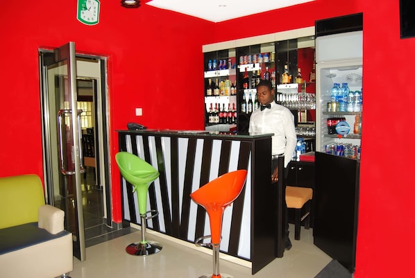 A bar area with a red wall, a refrigerator stocked with beverages, and two colorful bar stools.