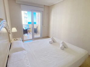 A hotel room with a large bed, a nightstand with a lamp, and a view of a balcony with outdoor furniture.