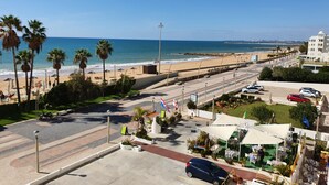 Une rue côtière bordée d’une plage, de palmiers et d’une rangée de voitures garées.