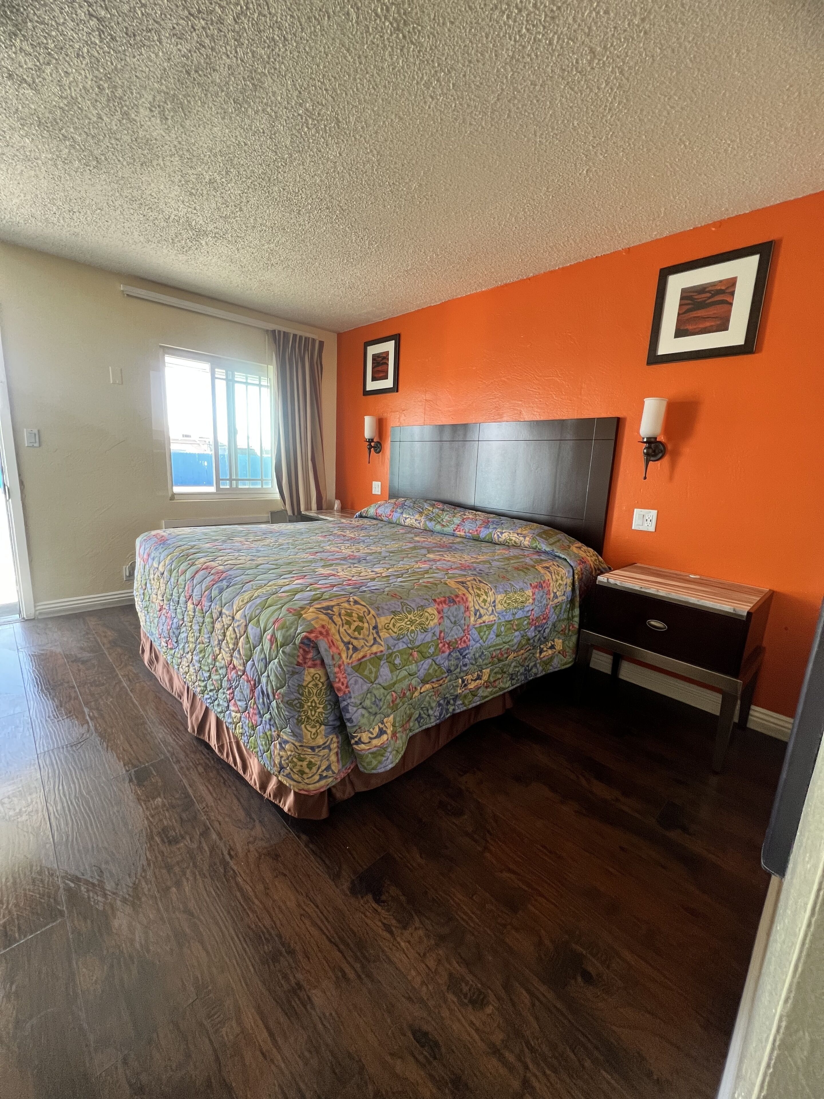 Une chambre avec un grand lit, une table de chevet, une fenêtre avec des rideaux et un mur orange.