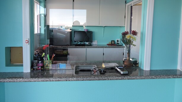 A kitchen with white cabinets, a countertop with various items, a computer, and a vase with flowers. - Walden Motel (Las Vegas)