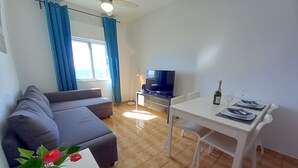 Un soggiorno moderno con un divano grigio, un tavolo da pranzo per due persone, una televisione e una ventola a soffitto.