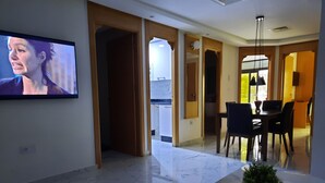 Una sala de estar moderna con un televisor de pantalla plana montado en la pared, piso de mármol y un comedor con mesa y sillas.