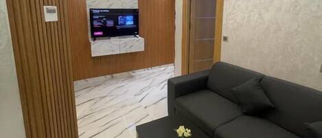 Un salon moderne avec un canapé d’angle, une table basse et un téléviseur fixé sur un mur recouvert de panneaux en bois.