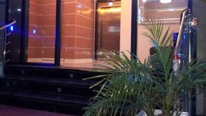 Entrada de hotel con alfombra roja, mostrador de recepción y cartel que indica zona de visitas.