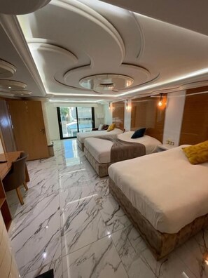 Habitación de hotel con piso de mármol, dos camas, un escritorio y vistas al exterior.