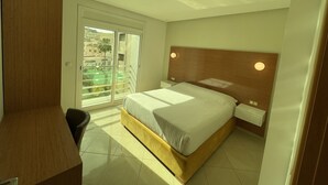 Un dormitorio con cama, escritorio y puerta corrediza de vidrio que da a un balcón.