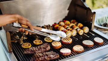 Une personne qui fait griller différents types de viande et de légumes sur un barbecue extérieur.