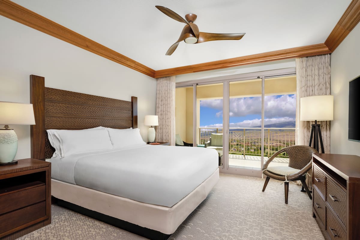 A hotel room with a large bed, a ceiling fan, a balcony with a view, and a TV.
