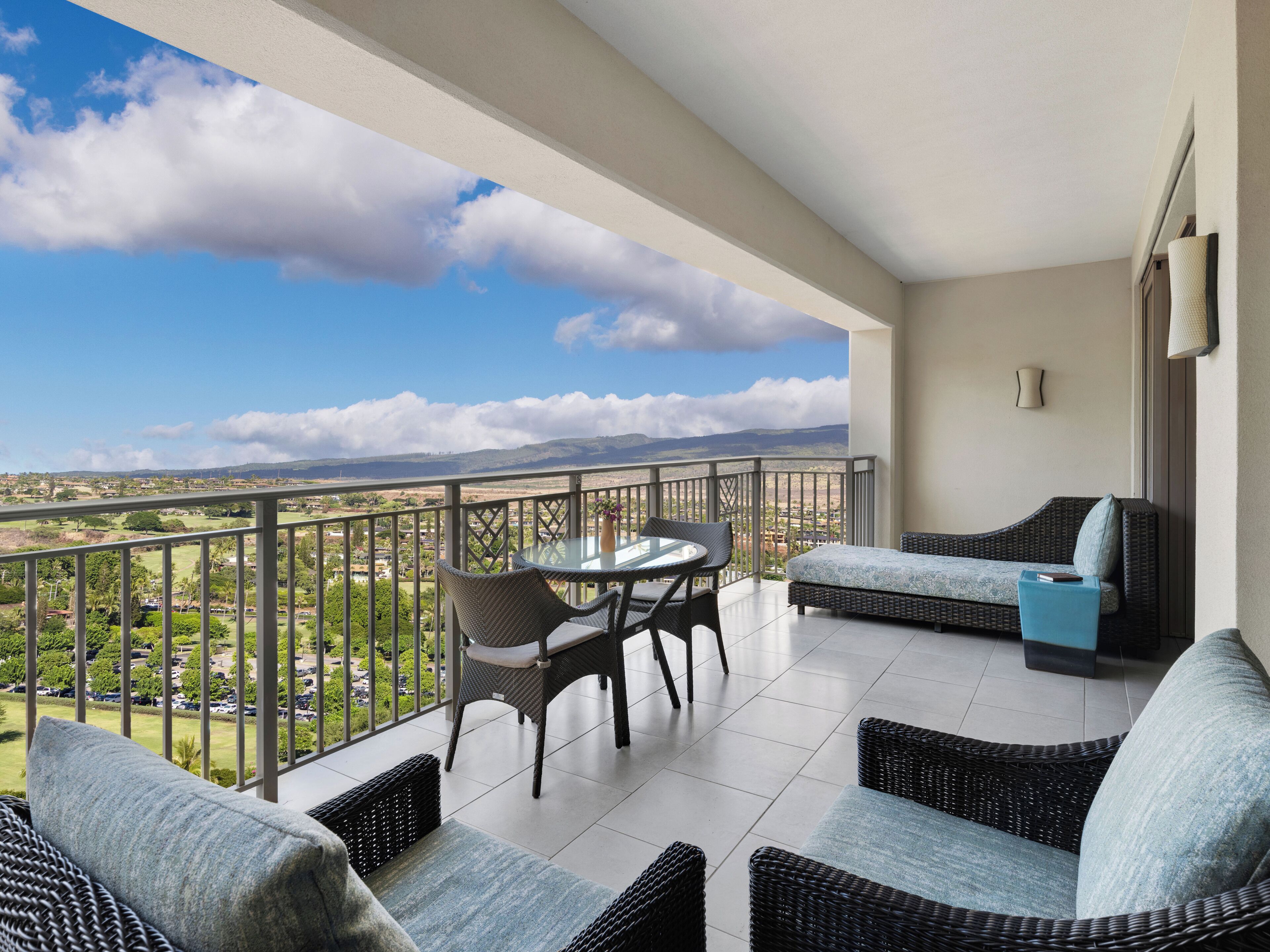 A balcony with wicker furniture, a glass table, and a view of a landscape.