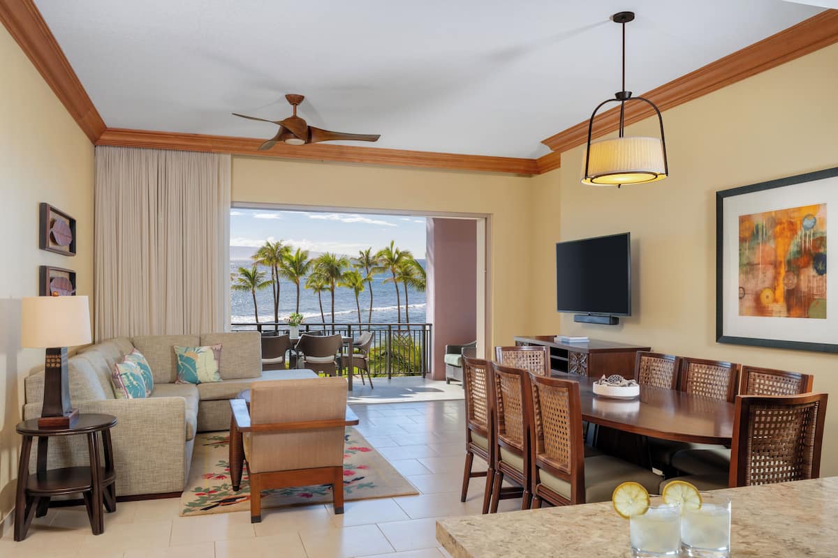 A hotel room with a balcony, a sofa, a dining table, and a TV.