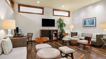 A modern living room with a flat-screen TV, comfortable seating, a bookshelf, and a potted plant.