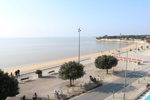 Eine Uferpromenade mit Sandstrand, Bäumen und freiem Blick auf das Meer.
