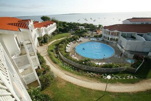 Ein Poolbereich mit freiem Blick auf das Meer, umgeben von einem weißen Gebäude mit Balkonen.