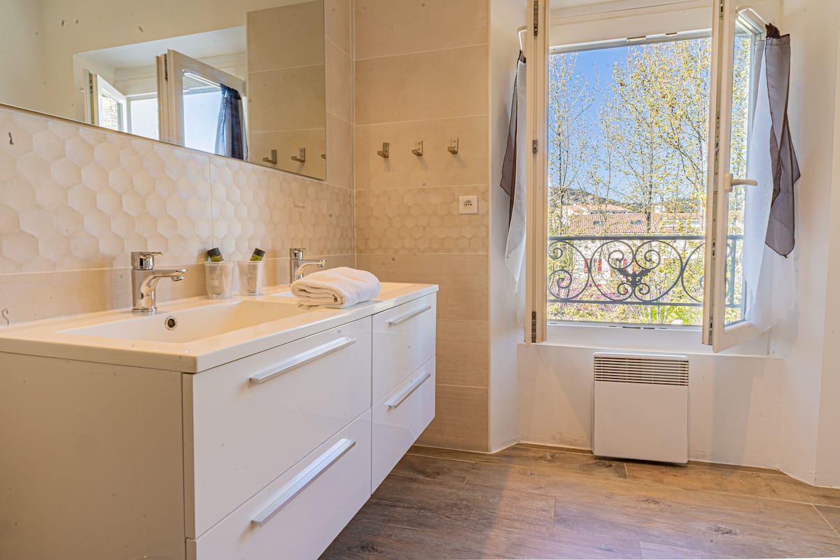 A bathroom with a white sink, mirror, and a window with a view of a balcony and trees.