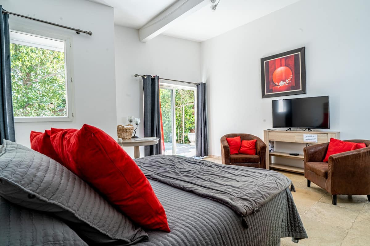 A hotel room with a bed, two armchairs, a TV, and a window with curtains.