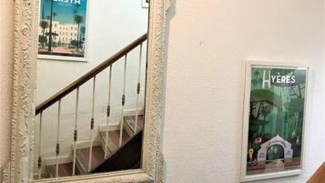 A mirror with an ornate frame reflecting a staircase and a poster of a tropical scene.