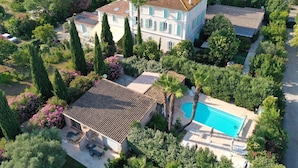 Una amplia villa con piscina, rodeada de exuberantes jardines y altos árboles.