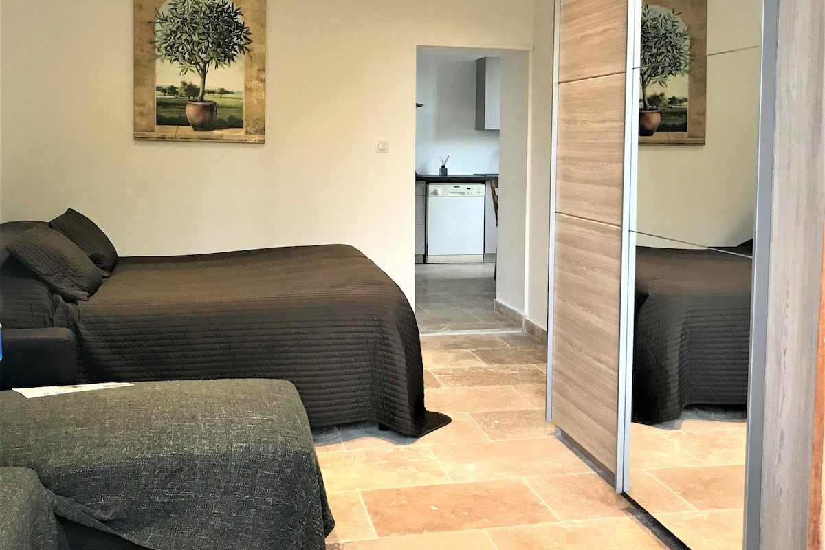 A bedroom with a bed, a bedside table, a mirror, and a painting of a tree.
