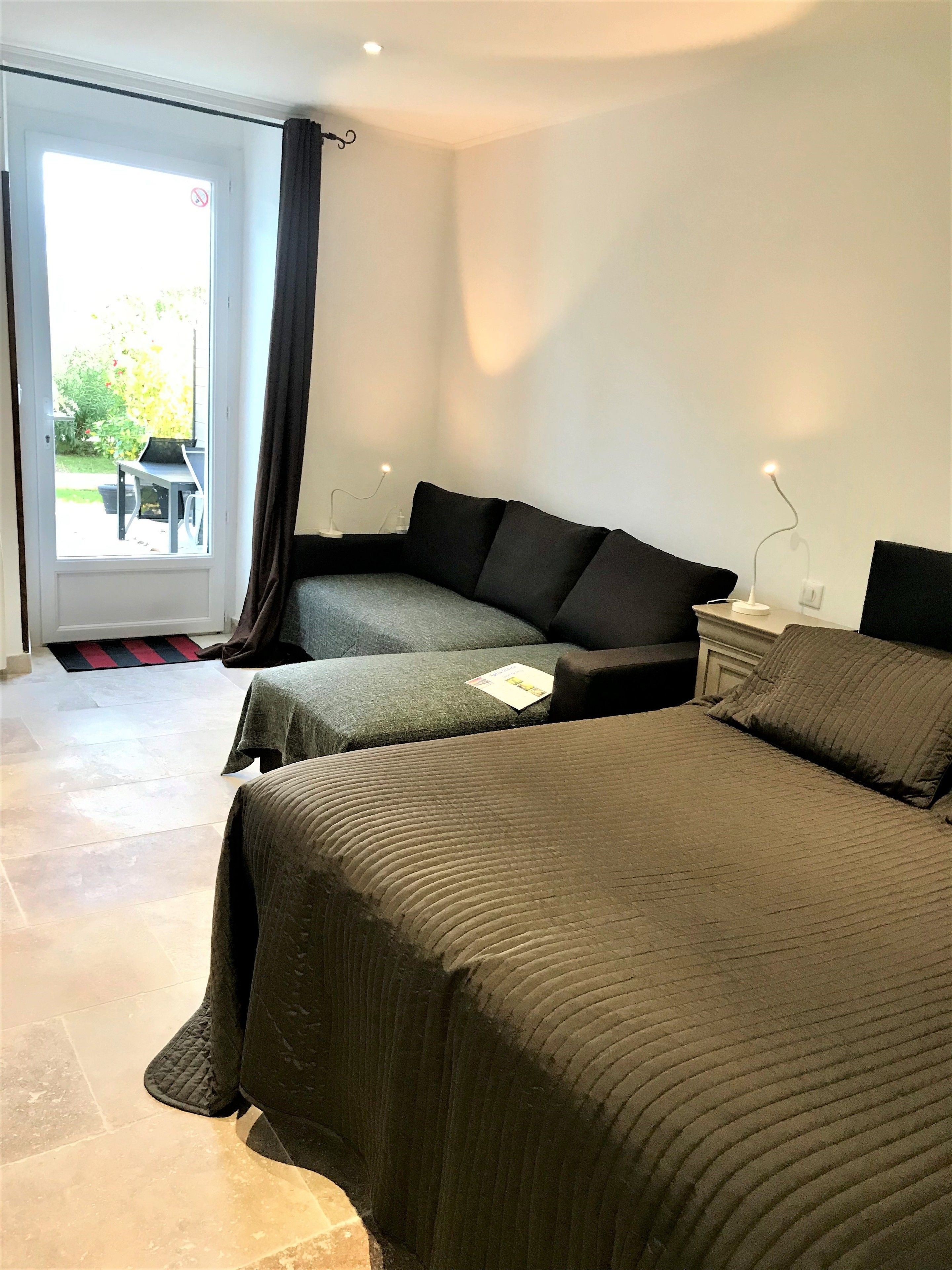 Un dormitorio con dos camas, una mesita, una silla y una puerta que da al exterior.