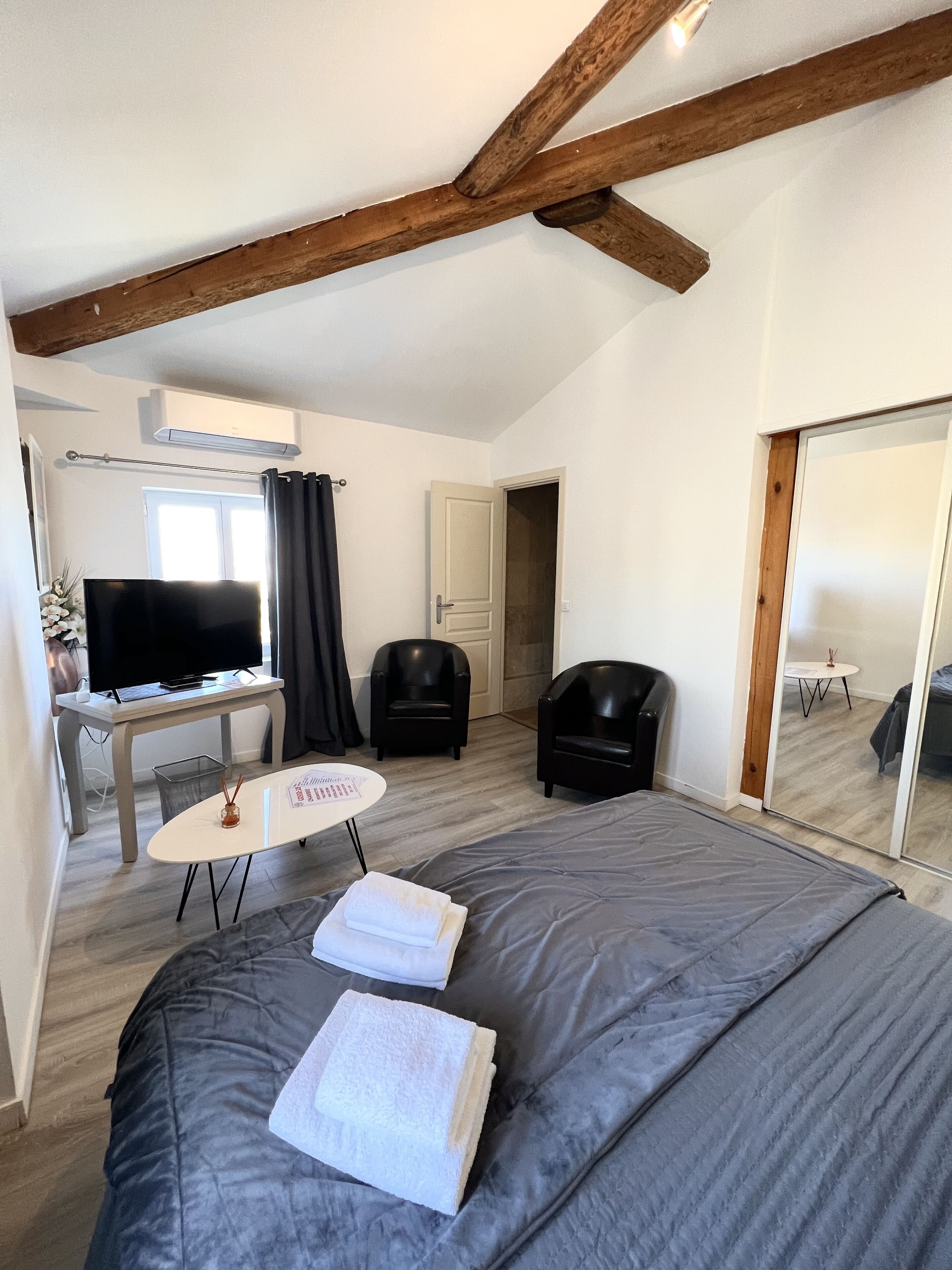 A modern bedroom with a large bed, a small table with a chair, a TV, and a mirror.