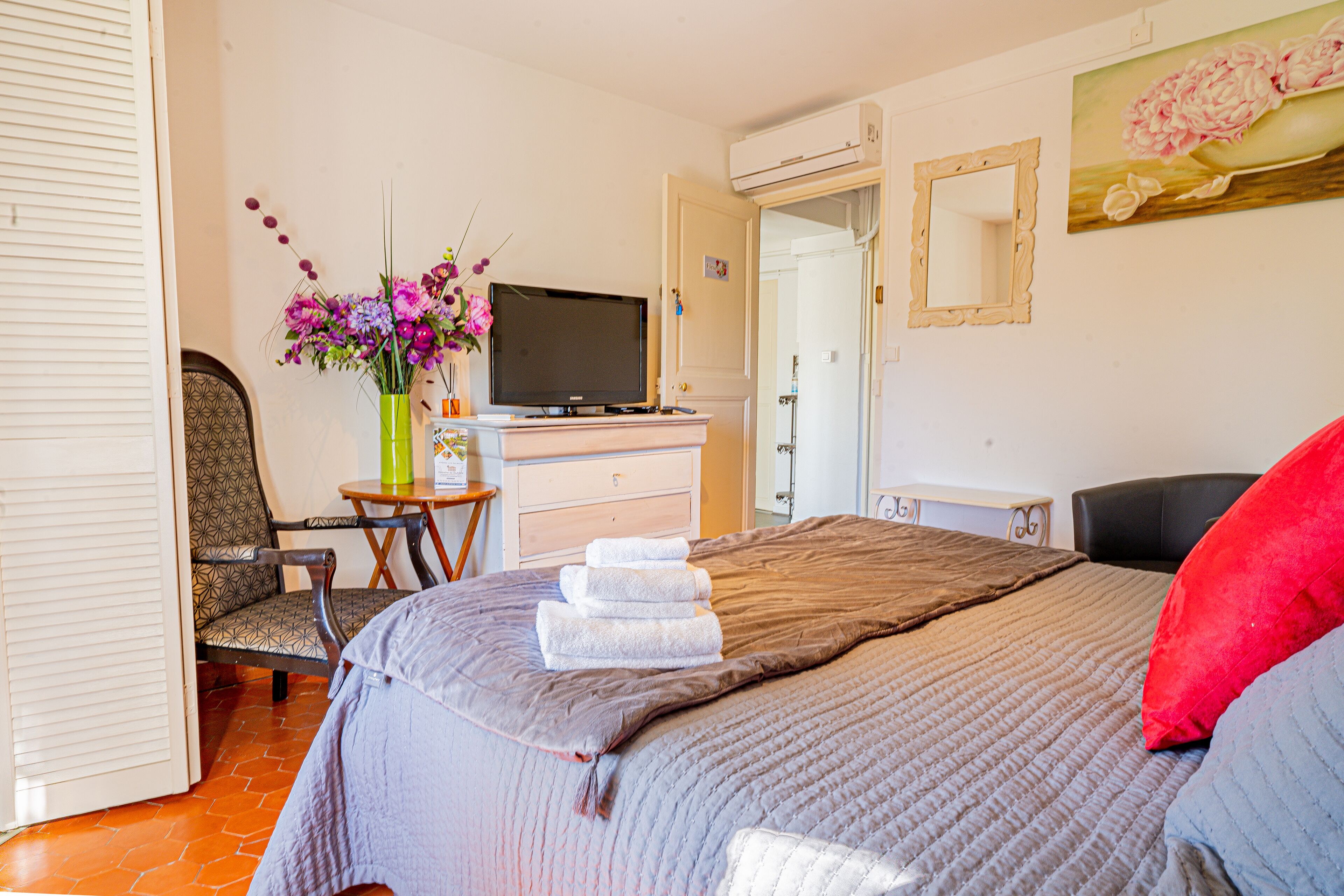Een hotelkamer met een bed, een stoel, een bureau met een computer, een televisie en een schilderij aan de muur.