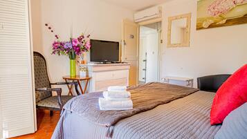 Een hotelkamer met een bed, een stoel, een bureau met een computer, een televisie en een schilderij aan de muur.