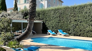 Zona de piscina con sillones reclinables y un edificio al fondo.