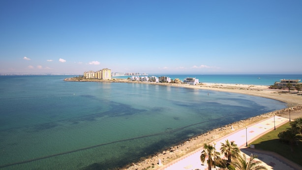 Um resort costeiro com vista clara para o mar, uma praia de areia e uma série de edifícios ao longo da costa.