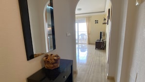 Um corredor com uma toucador preta, um espelho e uma cesta de objetos na parede. Há uma porta que dá para uma varanda com vista.