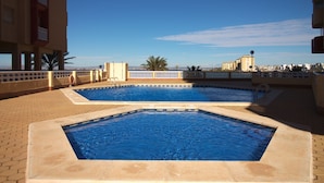 Piscina no terraço com duas áreas distintas, céu claro e vista distante de edifícios.
